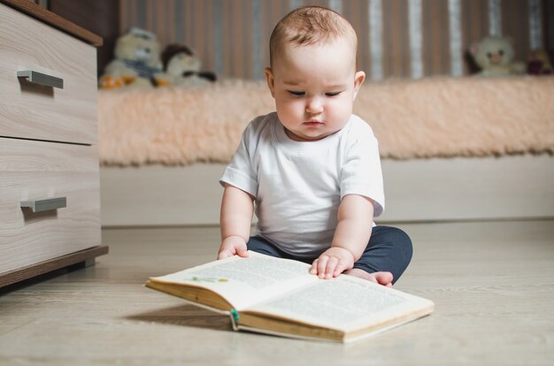 un bébé assis par terre lit un livre