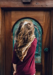 une petite fille aux cheveux long s'apprête à ouvrir une porte en bois