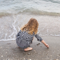 une petite fille accroupie les pieds dans l'eau près d'elle le sable et des coquillages