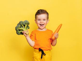 un petit garçon tenant dans une main un brocoli et dans l'autre une carotte