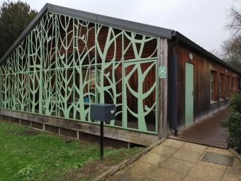 une sorte de chalet en bois avec un claustra vert en forme d'arbre