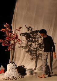 un homme pieds nus pr&egrave;s de 2 arbres et d'une montagne repr&eacute;sent&eacute; par un drap blanc